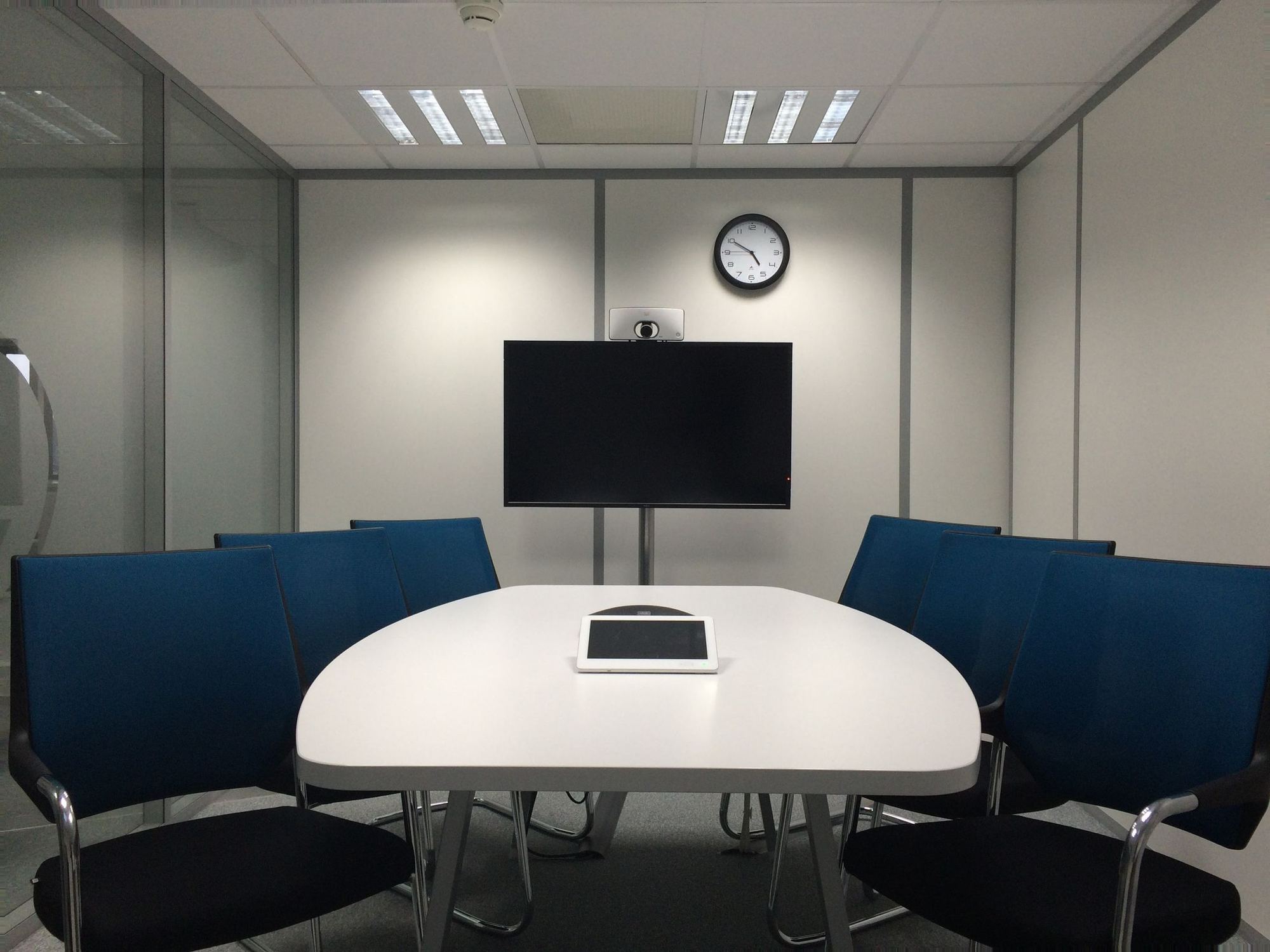 A meeting room with a conference table and a wall-mounted video conferencing screen