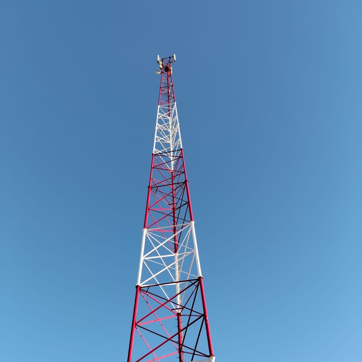 Red and white lattice telecom mast at Suez Wind Energy, seen from its base, with its antennas at the top